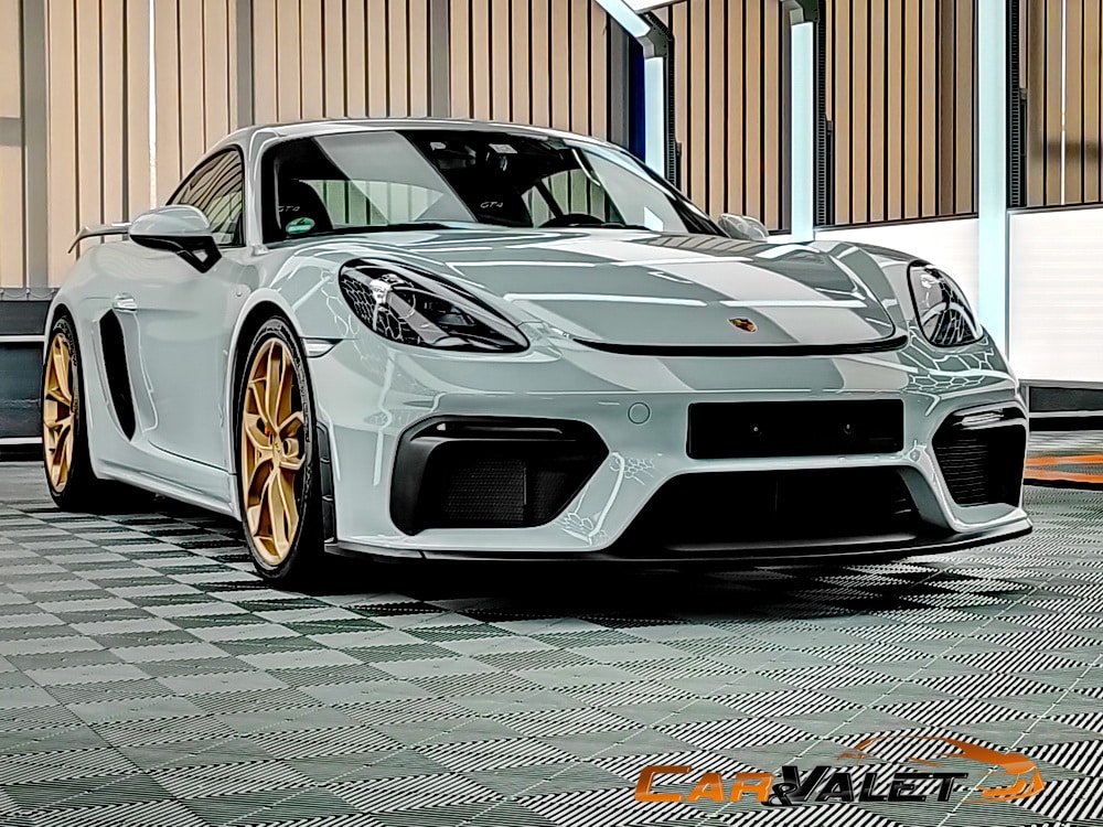 Weißer Porsche Cayman GT4 mit goldfarbenen Felgen im Lichttunnel.