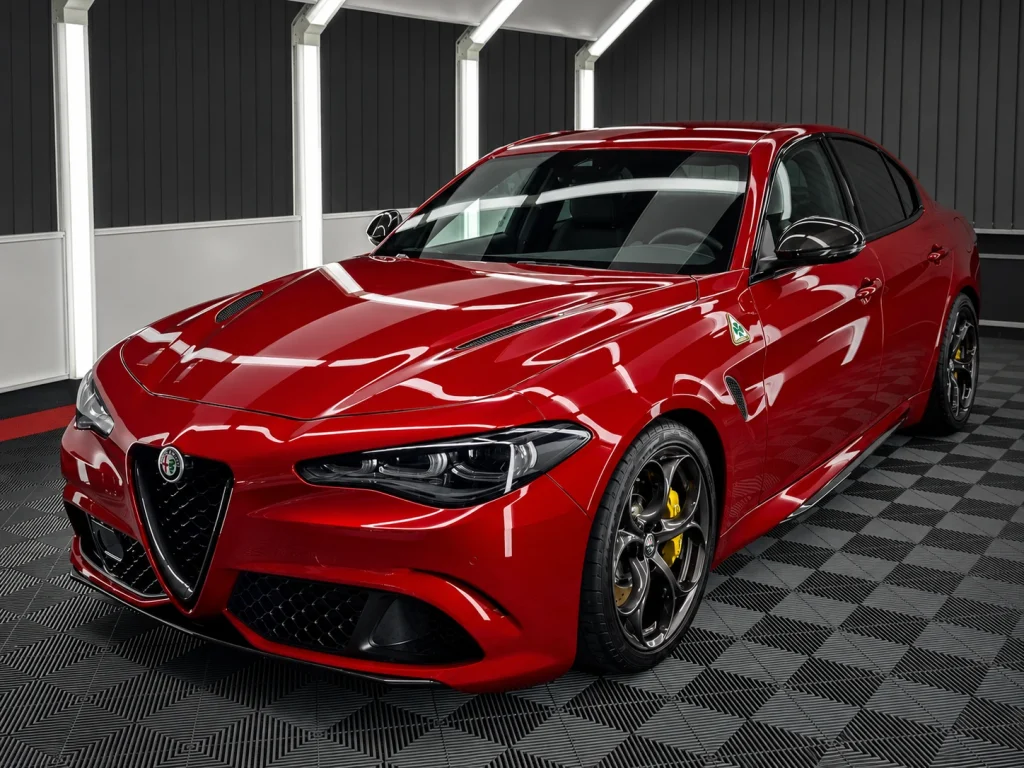 Rote Alfa Romeo Giulia mit dunklen Felgen, schräg von vorn im Lichttunnel von Car and Valet.